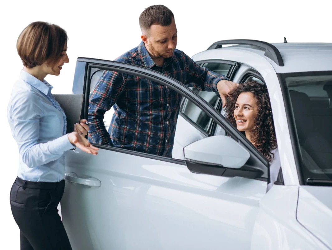 Casal feliz avaliando um carro branco enquanto conversa com uma vendedora em uma concessionária.